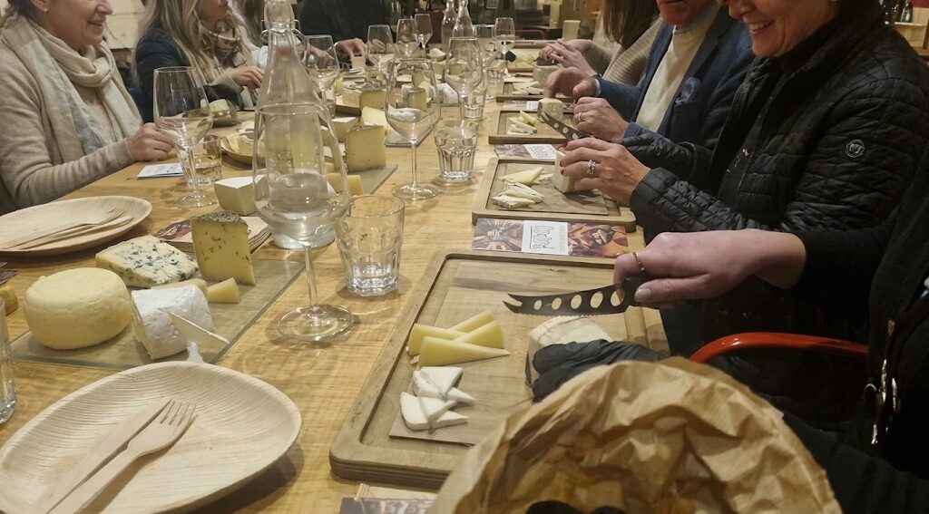 Partecipanti a una degustazione di formaggi seduti a una lunga tavolata in legno, con taglieri di formaggi stagionati, erborinati e freschi, coltello da formaggio e calici, a Testaccio, Roma.